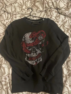 Svart Philipp Plein  - Säljer en svart Philipp Plein hoodie i storlek S (herr). Fick den som gåva men kommer tyvärr inte till användning hos mig. Den har en snygg och iögonfallande dödskalle med röda detaljer framtill som verkligen sticker ut. Den är använd och har lite slitage, men fortfarande i helt okej skick och funkar fint till vardags. Perfekt för dig som gillar en edgy stil. Packar noggrant och skickar samma dag om betalning sker tidigt, annars dagen efter. Hör av dig vid frågor!