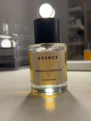 ESSNCE Absolu Vanilla Eau de Parfum - En stilren parfymflaska i glas med svart lock från ESSNCE. Doften heter Absolu Vanilla och är en Eau de Parfum. Perfekt för dig som gillar varma, söta dofter. Doften liknar Billie Ellish parfymen. Nästan helt full (alltså ungefär 50ml)