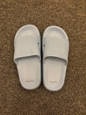 Sandaler/tofflor - Säljer ett par ljusblå slides från happy flops. Sandalerna har bred ribbad rem över foten och en mjuk, strukturerad sula för extra komfort. Tillverkade i lätt och tålig syntet