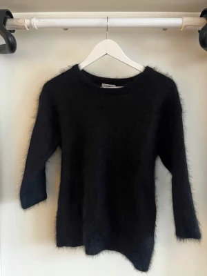 Svart fluffig trekvartsärmad tröja J.Lindeberg - Mysig svart stickad tröja från J.Lindeberg med fluffig yta och rund hals. Tröjan har trekvartsärmar 