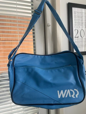 Blå axelväska från WARP - Snygg blå axelväska från WARP med justerbar axelrem och stort huvudfack. Väskan har en dragkedjeförsedd ytterficka, samt mindre ficka med dragkedja inuti.  Perfekt för att bära med sig det viktigaste till skolan eller stan. Lite slitage under ( se bilder) men annars en väldigt fin väska. 
