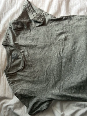 Grå basic t-shirt i bomull - En enkel grå t-shirt i mjuk bomull med rund hals, korta ärmar och polo logen nere åt vänster sida. Perfekt till jeans eller shorts för en clean och avslappnad stil. Klassisk passform och neutral färg som funkar till allt.