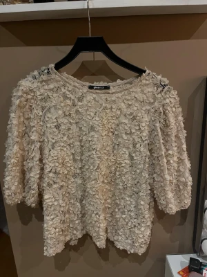Beige blommig blus från Gina Tricot - Supersöt beige blus från Gina Tricot med 3D-blommor över hela tyget. Blusen har rund halsringning och halvlånga ärmar. Perfekt för dig som vill sticka ut med en romantisk och trendig look.