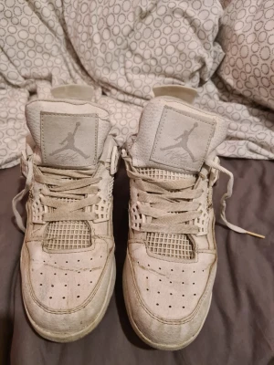 Vita Air Jordan 4 Retro sneakers - Snygga vita Air Jordan 4 Retro sneakers med klassisk Jumpman-logga på plös och häl. Skorna har meshpaneler, perforerad tå och detaljer i läder och textil. Ikonisk siluett med högt skaft och robust sula. Perfekta för dig som gillar streetwear och basketstil.