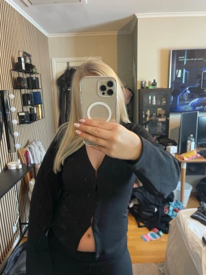 Svart ribbad kofta med v-ringning - Snygg svart kofta med v-ringning och knäppning framtill. Modellen är figurnära och har långa ärmar. Perfekt att styla med både jeans och kjol för en trendig look.