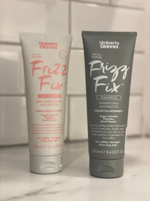 Umberto Giannini Frizz Fix duo - Säljer ett set med Umberto Giannini Frizz Fix shampoo och balsam, båda i tub om 250 ml. Shampoot är i en grå tub och balsamet i en ljusrosa tub. Båda är veganska och innehåller keratinpeptider för att motverka frissigt hår.