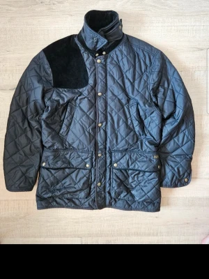 Svarta Raulp Lauren Jacka  - Hej, om du har nagra frågor om jacka meddelande mig.                                   Klassisk Quiltad Jacka från Polo Ralph Lauren (Kempton Model) Säljer en tidlös och stilren quiltad jacka från Polo Ralph Lauren i klassisk jaktstil ("Hunting style"). Detta är en av märkets mest ikoniska modeller, känd för sin kombination av funktionalitet och sofistikerad design. 