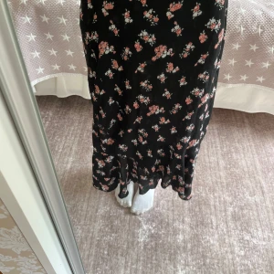 Svart blommig långkjol från 157 - Säljer denna supersöta svarta mellanlånga kjol med små rosa och vita blommor från Lager 157. Kjolen har volangdetaljer och ett mjukt, flowigt tyg med resår i midjan för skön passform. Inte använd mycket och inga defekter. Den är i storlek XS, hör av er om frågor!❤️(Säljer även på Vinted ifall man skulle vilja köpa där)