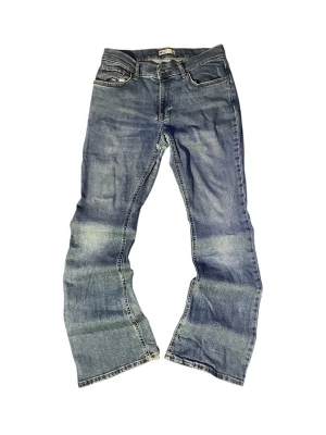Blå bootcut jeans från Levi's - Ett par klassiska blå bootcut jeans från Levi's med fem fickor och dragkedja. Jeansen har en snygg tvättad look med slitningar och bredare benslut. Perfekta för dig som gillar en avslappnad och retro stil.