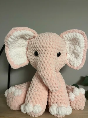 Rosa virkad elefant gosedjur - Supergullig virkad elefant i mjuk rosa och vit plysch. Elefanten har stora öron, svartglänsande ögon och detaljerade tassar. Perfekt som dekoration eller mysigt gosedjur. Handgjord känsla och unik design.