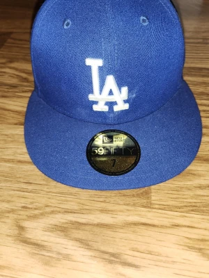 Blå LA 59FIFTY keps från New Era - Säljer en blå fitted keps från New Era, modell 59FIFTY, med LA Dodgers-logga broderad i vitt framtill. Klassisk rak skärm och officiell MLB-stämpel på insidan. Perfekt för dig som gillar streetwear och sportig stil.