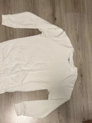 Vit långärmad tröja från Zara - En enkel och stilren vit långärmad tröja från Zara. Tröjan har rund halsringning och är gjord i mjukt bomullsmaterial. Perfekt för att matcha med jeans eller joggers. Klassisk design som funkar till många olika outfits.