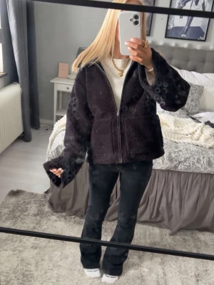 Svart teddyjacka med dragkedja - Mysig svart teddyjacka med dragkedja framtill och breda ärmar. Jackan har en avslappnad passform och är gjord i fluffigt teddy-material som ger en trendig look. Perfekt för att hålla värmen under kyliga dagar.