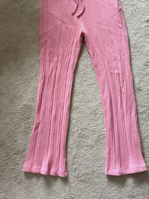 Rosa ribbade loungewear-byxor NA-KD - Mysiga loungewear-byxor från NA-KD i en härlig rosa färg. Byxorna har ribbad struktur, resår i midjan med dragsko och vida ben. Perfekta för chill dagar hemma eller när du vill vara extra bekväm.