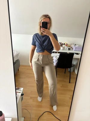 Beige kostymbyxor med raka ben - Snygga beige kostymbyxor med hög midja och raka ben. Byxorna har dragkedja och knapp framtill samt fickor på sidorna. Perfekta för en clean och stilren look. Materialet ser ut att vara mjukt och följsamt, vilket ger en bekväm passform. Passar S också. Nypris 500kr.
