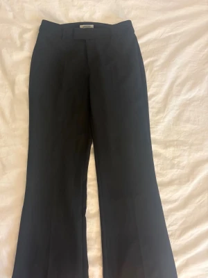 Svarta kostymbyxor från Madlady - Snygga svarta kostymbyxor från Madlady med klassisk rak passform och pressveck. Byxorna har hällor för skärp och är perfekta för en stilren look. Materialet känns mjukt och följsamt, vilket gör dem bekväma att bära hela dagen.