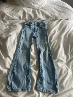 Ljusblå utsvängda jeans - Säljer ett par ljusblå jeans med utsvängda ben och klassisk femficksdesign. Jeansen har normal midja. Perfekta för dig som gillar en retroinspirerad look och vill ha ett par bekväma och trendiga jeans.
