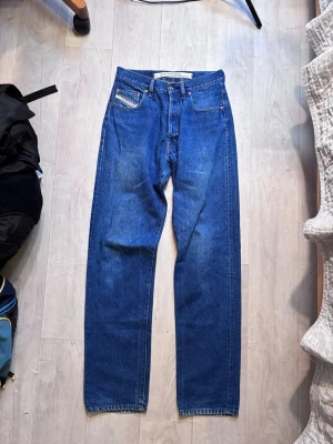 Diesel Industry blå jeans - Klassiska blå Diesel Industry jeans med rak passform och hög midja. Jeansen har fem fickor, knappgylf och är gjorda i slitstark bomullsdenim. Perfekta för en avslappnad och tidlös stil.