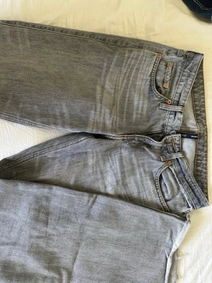 Arrow gråa jeans  - Säljer ett par grå jeans med arrow passform och klassisk femficksdesign. Jeansen har en ljusgrå tvätt, kopparfärgade nitar och rå kant vid benslutet för en trendig look. Perfekta för dig som gillar en avslappnad stil.