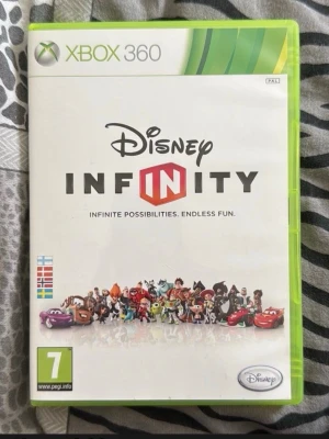 Disney Infinity till Xbox 360 - Disney Infinity till Xbox 360 är ett äventyrsspel där du kan utforska olika världar med kända Disney- och Pixar-karaktärer. Omslaget är vitt med färgglada figurer och spelet har en grön plastbox. Perfekt för dig som gillar kreativitet och action.