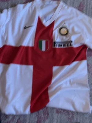 Inter Milan Ibrahimovic matchtröja - Säljer en vit Inter Milan matchtröja från Nike med röd korsdesign, klubbmärke och Pirelli-logga på bröstet. På ryggen står Ibrahimovic och nummer 8 i blått. Perfekt för dig som älskar fotboll och vill ha en ikonisk supportertröja.