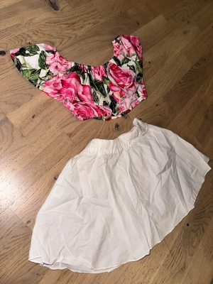 Blommig offshoulder topp - Söt offshoulder topp med stora rosa och röda rosor samt gröna blad på vit botten. Toppen har korta, vida ärmar och en croppad passform. Perfekt för sommarens varma dagar och ger en fin vibe.