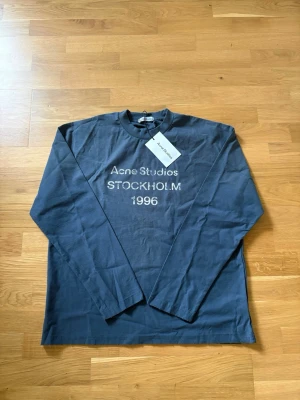 Mörkblå långärmad topp Acne Studios - Snygg mörkblå långärmad topp från Acne Studios med tryck 'Acne Studios STOCKHOLM 1996' på bröstet. Klassisk rund halsringning och mjukt bomullsmaterial. Perfekt för en clean och stilren look.