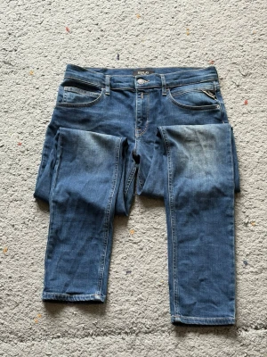 Blå jeans från Replay - Snygga blå jeans från Replay med klassisk femficksdesign och diskreta slitningar på låren. Jeansen har raka ben och tydliga kontrastsömmar. Perfekta för en avslappnad och trendig look.