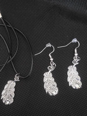 Handgjort Smyckeset med silverfärgade löv - Snyggt handgjort  smyckeset med halsband och örhängen i silverfärg med lövformade hängen dekorerade med gnistrande stenar. Halsbandet har svart band och justerbart spänne. Perfekt för dig som gillar detaljer och bling.
