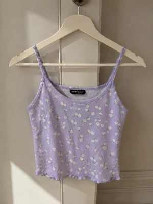 Ljuslila blommig linnetopp från SHEIN - Supersöt ljuslila linnetopp från SHEIN med små vita blommor och gröna detaljer. Toppen har smala axelband, ribbad struktur och en croppad passform. Perfekt för varma dagar och enkel att styla med jeans eller kjol.