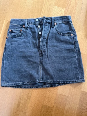 Grå jeanskjol Levi’s - Levi’s grå jeanskjol med knappgylf. Nästan oanvänd. Stl. 26. Köparen betalar frakt. 