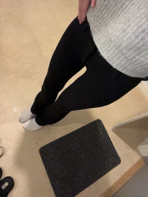 Svarta Lågmidjade  bootcut kostymbyxor  - Säljer ett par svarta  kostymbyxor bootcut med låg  midja och stretchigt material. Byxorna har en smal passform upptill och blir vidare nedtill vid benen. Perfekta till en stickad tröja eller crop top. OBS! Utan fickor , spegeln e smutsig så inga fläckar på byxorna 