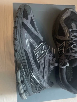 New Balance 1906R svarta sneakers - Svarta New Balance 1906R sneakers med mesh och syntetmaterial, coola detaljer i grått och silver samt klassisk N-logga på sidan. Skorna har en chunky sula och snörning framtill, perfekt för dig som gillar sportig och modern stil.