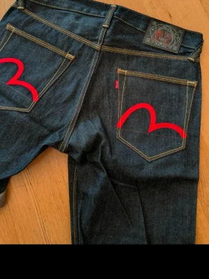 Mörkblå jeansshorts från Evisu - Snygga mörkblå jeansshorts från Evisu med klassiska röda måsmärken på bakfickorna. Shortsen har kontrastsömmar, uppvikta benslut och en midwaist passform. perfekta för dig som gillar streetwear.
