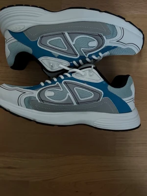 B30 blå grå och vit - Snygga sneakers i blått, grått och vitt med coola detaljer och tjock vit sula. Ovandelen är i mesh och syntetmaterial med vita skosnören och svart insida. Perfekta för dig som vill ha en modern och sportig look.
