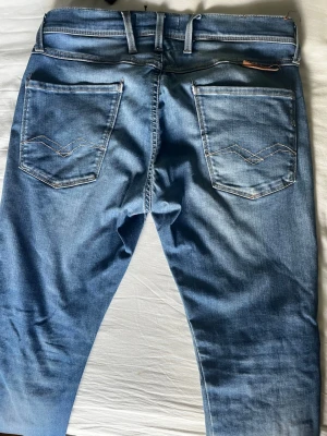 Blå jeans från Replay - Säljer ett par snygga blå jeans från Replay med klassisk femficksmodell och ljus tvätt. Jeansen har raka ben, kontrastsömmar och detaljerade bakfickor med broderi. Materialet är mjukt denim i bomull med lite stretch för extra komfort.