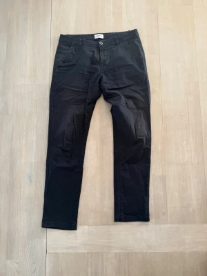 Blå chinos med rak passform - Snygga chinos med rak passform och klassisk design. Byxorna har två sidofickor och knappgylf. Perfekta för en clean och stilren look. Materialet känns mjukt och följsamt, vilket gör dem bekväma att bära hela dagen.