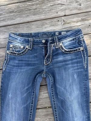 Miss Me blå jeans med ”diamanter”och brodyr - Säljer ett par blå Miss Me jeans med snygga  slitningar, kontrastsömmar och coola nitar på fickorna. Både fram- och bakfickor har broderade detaljer och dekorativa knappar. Perfekta för dig som gillar statement-jeans med unik design. Är i superfint skick! Som xs i storlek 