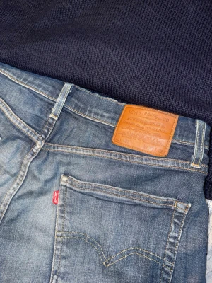 Blå Levi's jeans med klassisk passform - Ett par blå jeans från Levi's med klassisk femficksmodell och raka ben. Jeansen har en snygg tvättad look, detaljer i kopparfärg och det ikoniska läderpatchen bak i midjan. Tillverkade i slitstark denim med den röda Levi's-taggen på bakfickan. Byxorna kan kännas som större än vad det står men är ju upp till personen