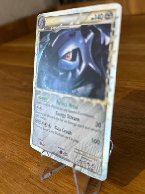 Steelix Pokémonkort holografiskt - Säljer ett holografiskt Steelix Pokémonkort med silverfärgad ram och coolt motiv av Steelix. Kortet har detaljer i metallic och text på engelska med attacker som Energy Stream och Gaia Crush. Perfekt för samlare eller Pokémonfans.