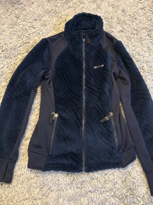 Mörkblå fleecejacka från JH Collection - Mysig mörkblå fleecejacka från JH Collection med dragkedja framtill och två fickor med dragkedja. Jackan har hög krage och är perfekt för kyliga dagar. Snygg och sportig design med mjukt material och tumhål vid ärmslut. Inte synligt använd. 