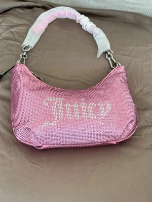 Glittrig rosa axelväska Juicy Couture - Superfin ljusrosa handväska i strass / kristaller från Juicy Couture. Väskan kommer med tillhörande portmonnä och ett extra väskrem (axelrem). 