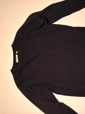 Svart tröja från RYVLS Stockholm - En stilren svart tröja från RYVLS Stockholm med rund halsringning och långa ärmar. Tröjan har ribbade muddar vid hals, ärmslut och nederkant. Perfekt basplagg för en clean och enkel look.