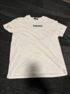 Vit DSQUARED2 t-shirt - Säljer en clean vit t-shirt från DSQUARED2 med svart logga tryckt på bröstet. Minimal design vilket passar med allt. Inte mycket använd, skön t-shirt att ha nu mot sommaren. Hör av er vid frågor!