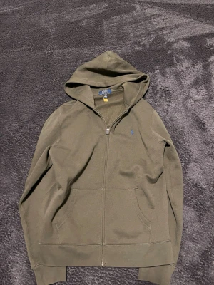 Olivgrön hoodie från Polo Ralph Lauren - Snygg olivgrön hoodie från Polo Ralph Lauren med dragkedja framtill och klassisk huva. Inte mycket använd, fin färg som man inte ser så jätteofta. Hör av er vid frågor!