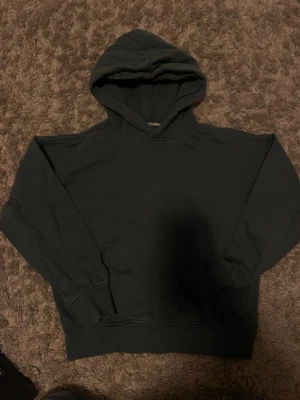 Mörkgrön basic hoodie med huva storlek 146-152 Kappahl  - En enkel och stilren mörkgrön hoodie med huva och magficka. Hoodien har ribbade muddar vid ärmslut och nederkant. Perfekt för en avslappnad look och passar till det mesta. Tillverkad i mjukt bomullsmaterial. Storlek 146-152
