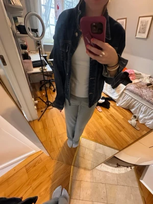 Mörkblå klassisk jeansjacka - Säljer en mörkblå jeansjacka med klassisk passform och silverfärgade knappar. Jackan har två bröstfickor med lock och knapp samt tydliga sömmar framtill. Perfekt att slänga över en hoodie eller t-shirt för en avslappnad look.