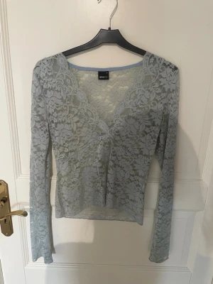 Ljusblå spetsblus från Gina Tricot - Säljer en ljusblå långärmad spetsblus från Gina Tricot. Blusen har v-ringning och är helt i genombruten spets med blommigt mönster. 