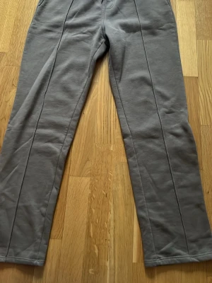 Grå mjukisbyxor med raka ben - Säljer ett par grå mjukisbyxor med raka ben och dekorativa sömmar framtill. Byxorna har resår i midjan och en bakficka. Perfekta för chill dagar eller när du vill vara bekväm men ändå se stilren ut.