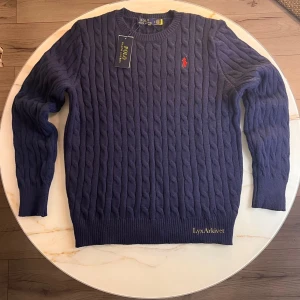 Polo Ralph Lauren kabelstickad tröja mörkblå - Klassisk kabelstickad tröja från Polo Ralph Lauren i marinblå färg. Mjuk och bekväm kvalitet med rund halsen. Passar grisch stilen                                                                         Storlek M                                                               Skick 10/10 